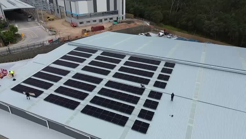 Aerial view of a commercial solar array being installed on a metal warehouse roof at Carole Park.