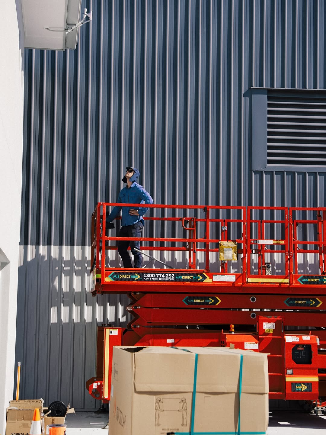 A Becka Electrical worker on a red scissor lift inspecting the exterior of a commercial building.