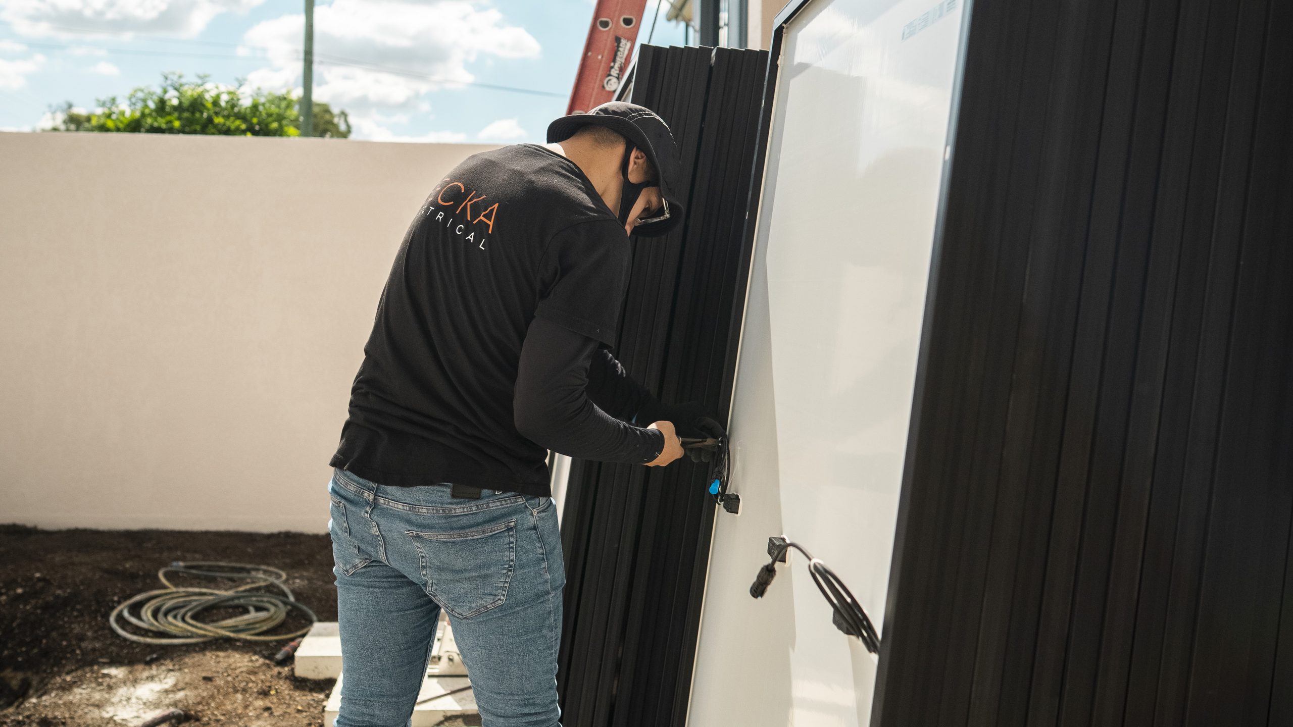 Becka electrician carrying a solar panel along a job site wall.