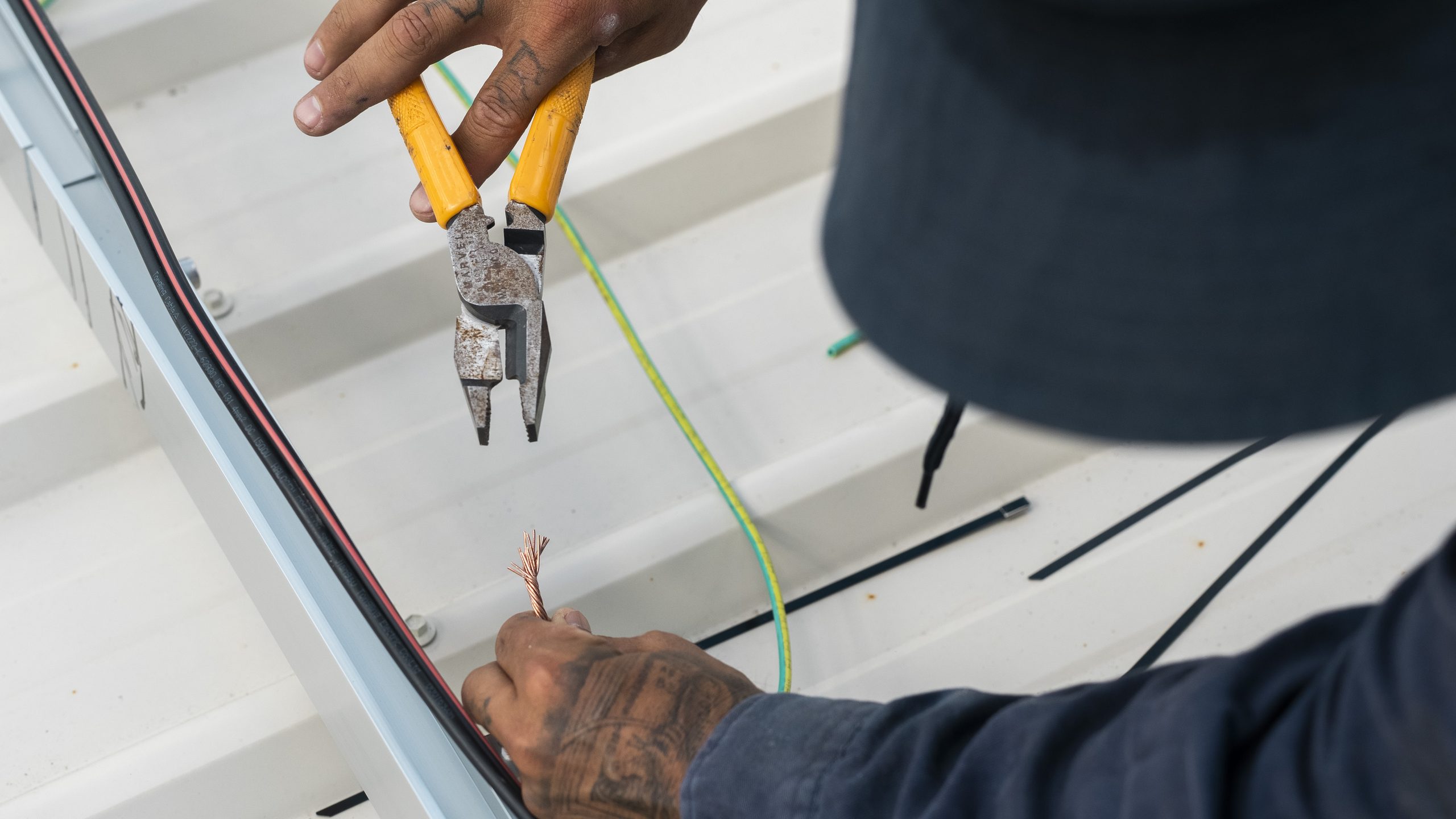 Close-up of an electrician's hands preparing wiring on a roof rail.