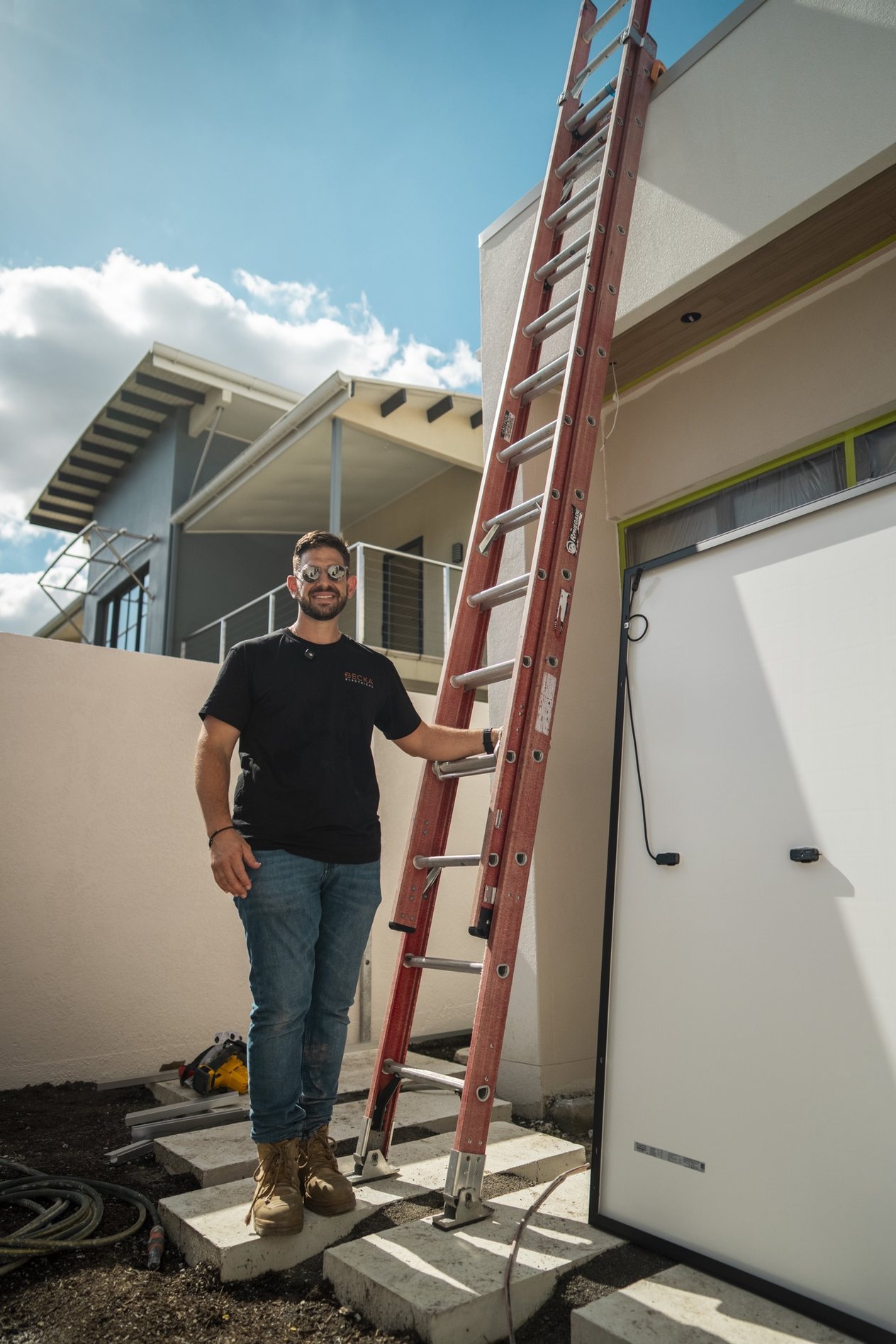 A Becka Electrical electrician standing at a ladder beside a solar panel during a home installation